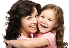 Mujer sujeta en brazos a su hija adoptiva, ambas están sonriendo.
