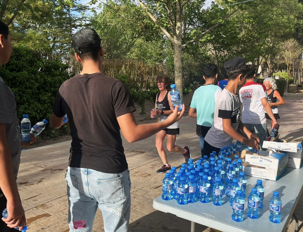 Los cinco jóvenes reparten botellas de agua a las personas participantes