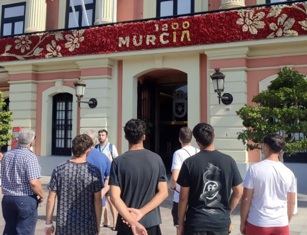 Varios jóvenes escuchan la explicación del guía turístico frente a la fachada del Ayuntamiento de Murcia