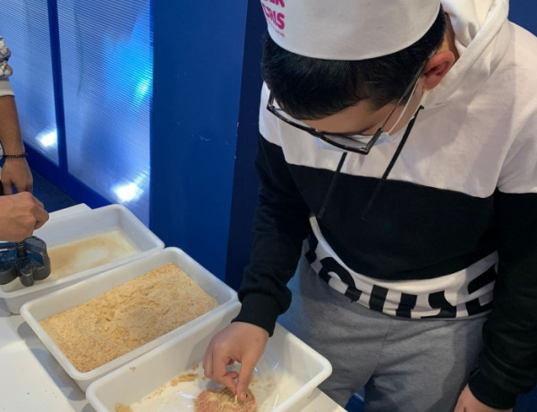 Un joven con gorro de cocina empana un trozo de carne