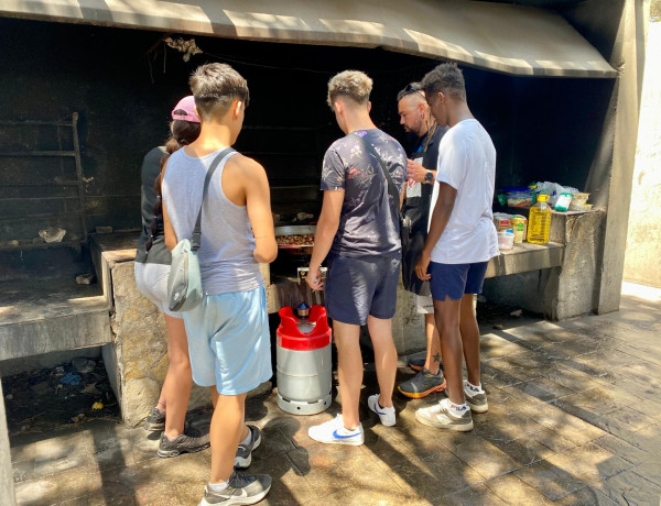 Varias personas jóvenes aprenden a manejar una barbacoa con un educador de Pi Gros