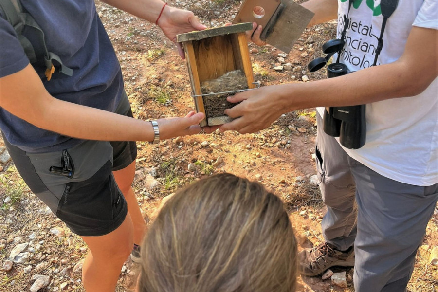 Dos profesionales del paraje muestran una de las cajas nido a una menor de la residencia