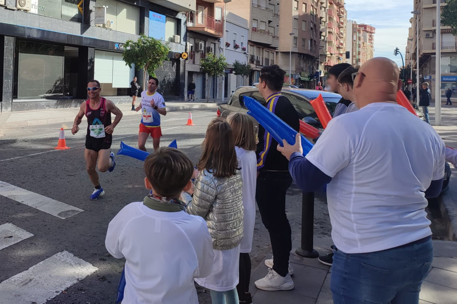 Los niños, niñas y adolescentes de los hogares, junto a un educador, animan a los corredores de la media maratón