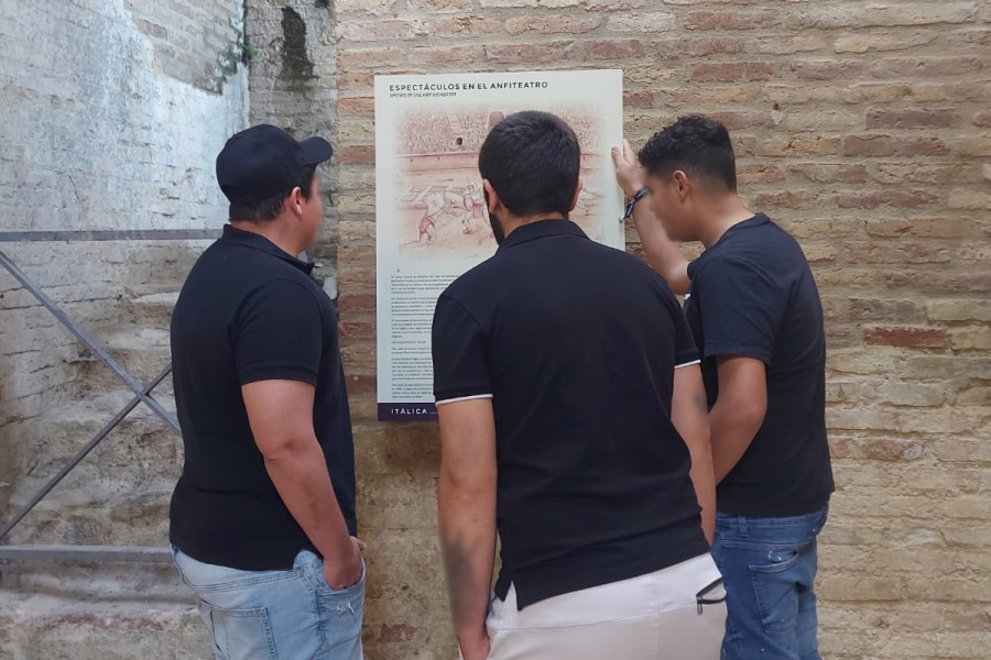 Tres jóvenes leen el panel informativo del anfiteatro romano