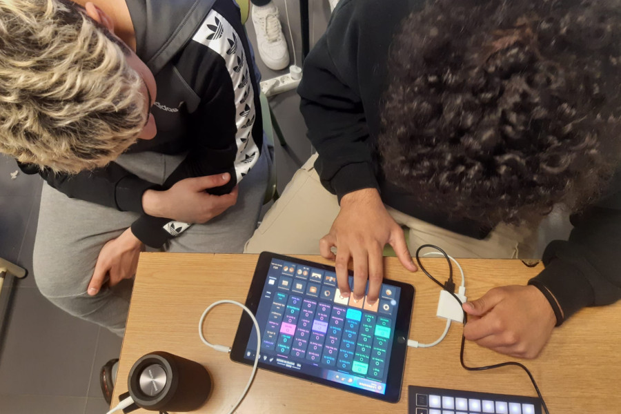 Dos jóvenes manejan la mesa de mezclas y la tablet para componer un tema