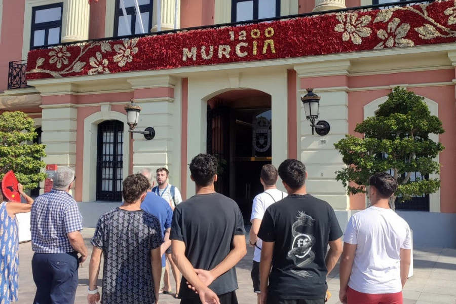 Varios jóvenes escuchan la explicación del guía turístico frente a la fachada del Ayuntamiento de Murcia