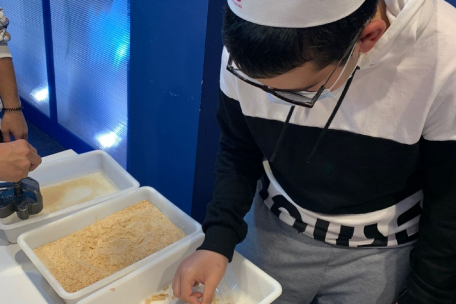 Un joven con gorro de cocina empana un trozo de carne