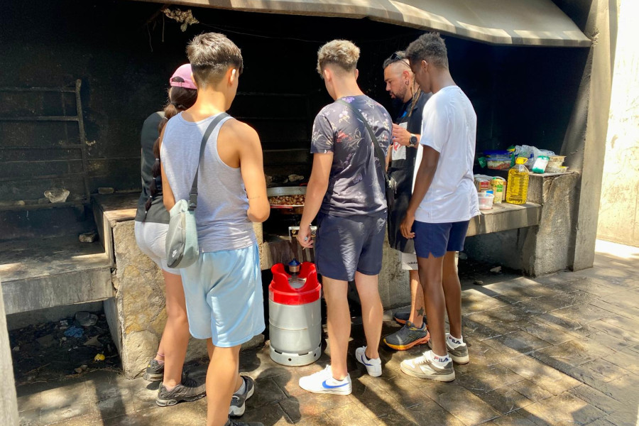 Varias personas jóvenes aprenden a manejar una barbacoa con un educador de Pi Gros